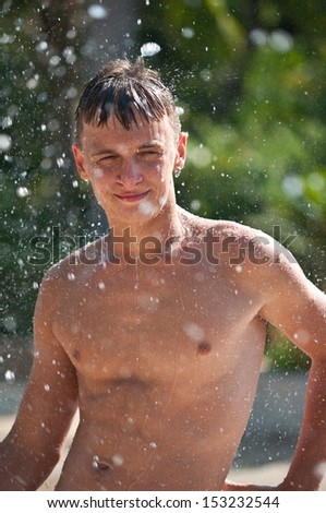 Wet teen in the spray of a fountain in a water park .