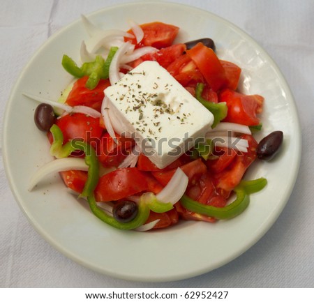 Greek salad on a plate with fresh veggies and feta cheese .