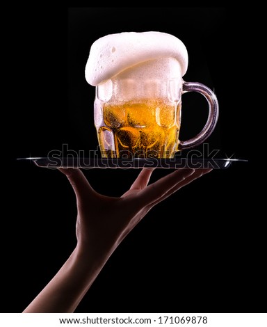 waiter hand and tray with Beer into glass on a black