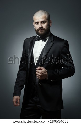 Stylish and brutal bald man with a beard in elegant black suit