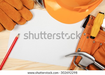Hard hat, hammer, pliers, nails, red pencil, work gloves and other tools isolated on a wooden background.