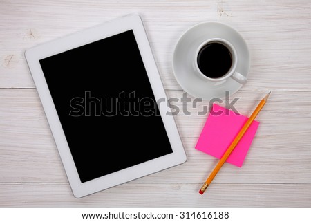 Workplace with hands holding blank digital tablet, pink notepad with yellow pencil and cup of coffee on wooden background. Above view shot.