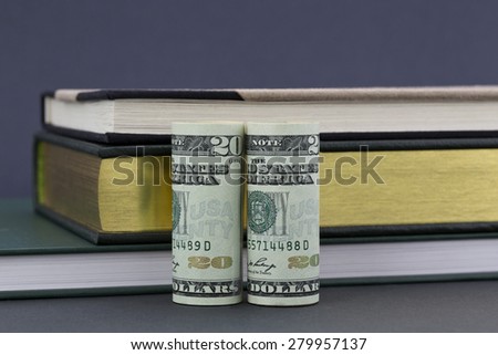 Costs and financing of education questions reflected by American currency placed with books on gray background.