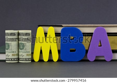 Graduate degree MBA letters with dollar currency in front of books on gray background.  Advance degree is a education business investment in critical skills.