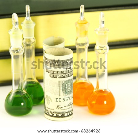 Four lab beakers site with rolled American dollar currency in front of  books and lab research journal