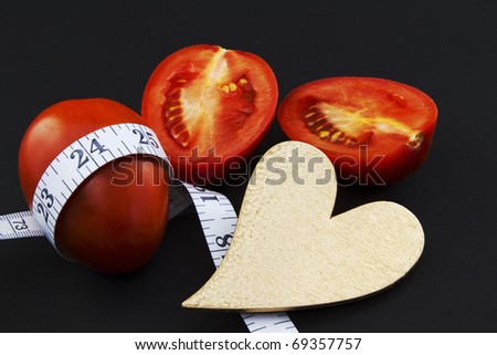 Gold heart with ripe, red plum tomatoes, whole and sliced, with measuring tape around waist of one tomato
