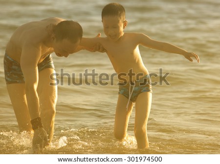 Asian father and son playing in the sea  at sunset