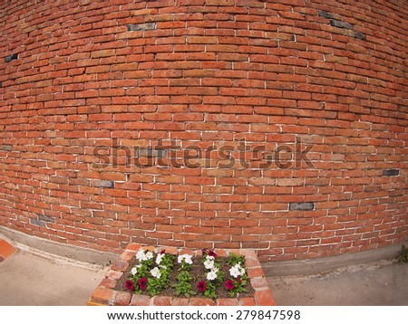 Stone wall of old red bricks and a small flower bed in front with wide-shots distortion view