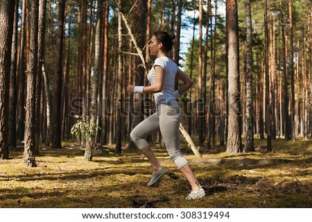 Young fitness woman running and jumping over logs while on extreme outdoor fitness training in forest.Fitness girl jumping exercising outdoors doing jump squats in forest.