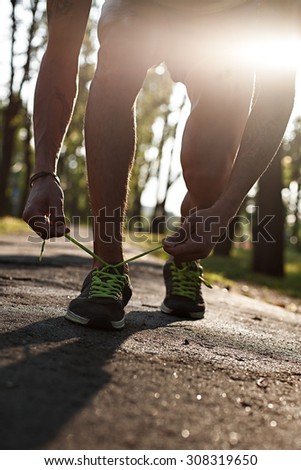 Running man closeup of running shoes on sunset or sunrise. Runner feet. Male sport fitness runner tying the laces of his shoes. Man fitness jog workout wellness on forest background.