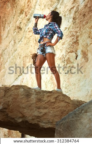 Slim, muscular girl standing on the precipice of rock and drinking water in Grand Canyon Crimea. Beautiful brunette asian young woman tourist travel in drinking water. The picture brunette young girl.