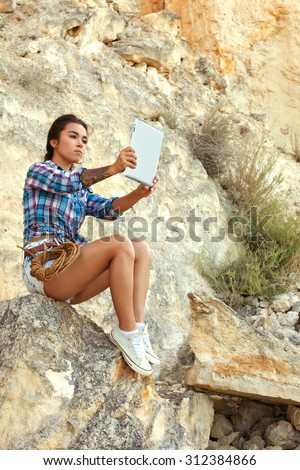 Hiking beautiful young girl resting in the mountains in the hands holding the tablet. Beautiful asian model in the mountains doing selfie.