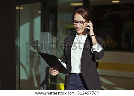 Business people concept- image of a business woman who goes out of office, talking on the phone with the documents in the hands. Beautiful business lady manager with documents.
