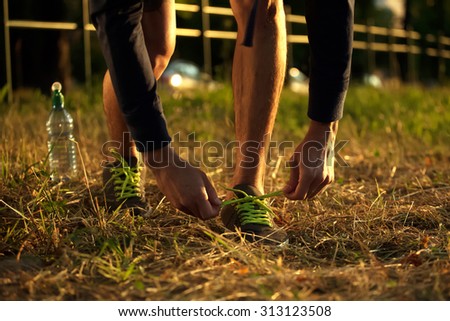 Athletic fit young sport fitness man model tying shoe laces. Image of runner shoes on grass in park.
