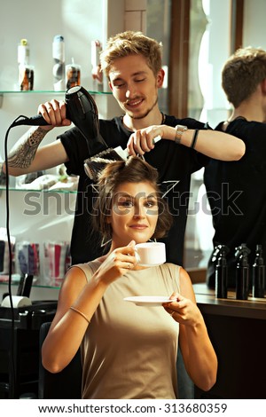 Concept satisfied and happy customer. Fashionable hair stylist makes a fashionable hairstyle client the young girl while she drinks tea or coffee and smiling- stock photo.