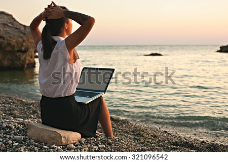 Young beautiful business woman dreaming of freedom and rest on the beach near the sea. Picture of working day the downshifting girl on the beach by the sea on the background of the beautiful nature.