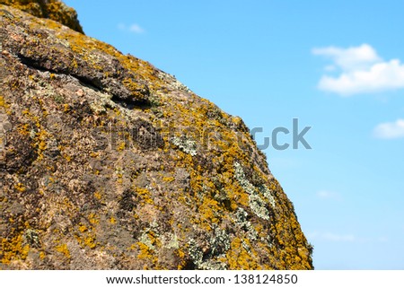 Lichen and moss on old granite rock taken closeup against of blue sky.
