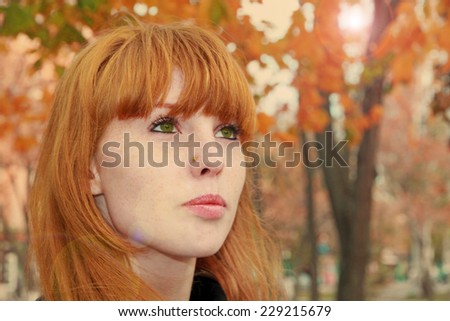 Pretty red hair girl face with freckles against red autumn foliage.Tonal correction.