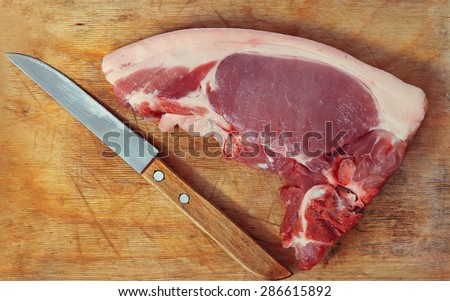 Raw pork meat and knife on wooden cutting board taken closeup.