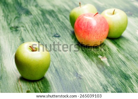 Green apple on the table, against the background of a red apple, side view