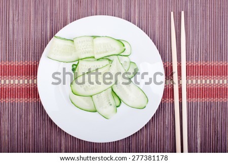Japanese cucumber salad with thinly sliced cucumbers in white plate Japanese shelves, lies on  dark straw view from above