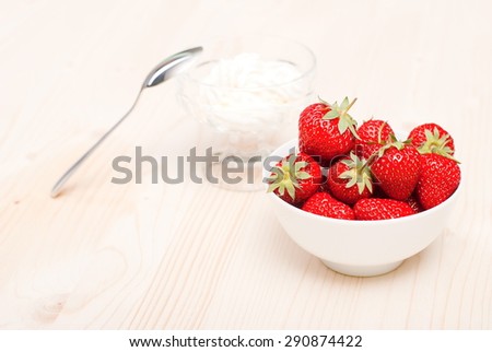 Strawberries in a white bowl on  light table, on the background of the cream in a transparent vase with spoon