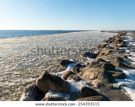 frozen beach near shipyard and sea port with rays of sun and wavebreaker