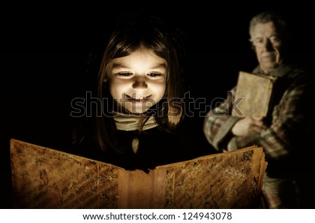 Young girl reading a very old book with grandfather in the background