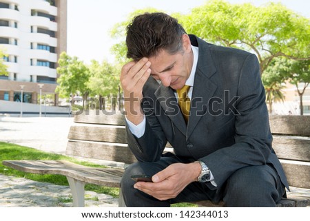 Worried businessman in a park bench with cellphone