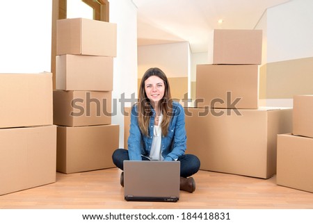 Beautiful girl with laptop and cardboard boxes unpacking in new home
