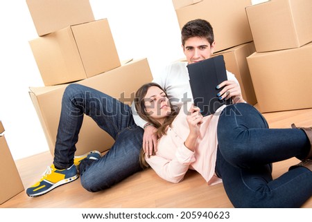 Happy couple with tablet and boxes moving into new home apartment