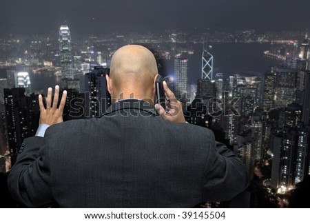 Businessman back, making a call by cellphone looking at the busy city lights, from his office