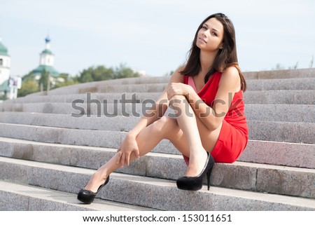 Young beautiful girl in a red dress sitting on steps