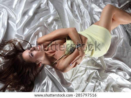 woman in bed on white satin. beautiful makeup, sexy  dress. long hair, long legs, large breasts. satin bedding