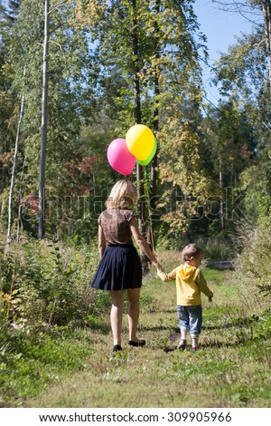 beautiful young mother walking with her young son in the forest with balloons