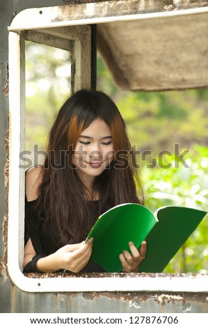 Asian woman reading at window of old train room .