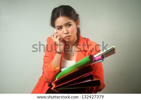 Busy Asian business woman with a lot of folders and colorful papers,calling by phone on background.