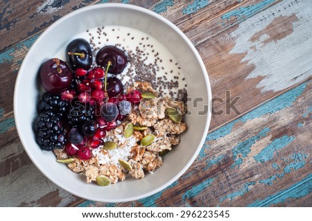 Healthy home made oatmeal porridge muesli with kefir yogurt and topped with blackberries, cherries,pomegranate, pumpkin and chia seeds. Served on a rustic wooden table.