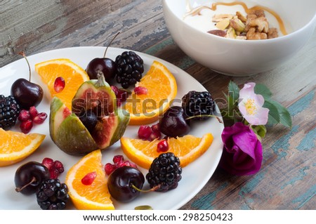 HeHealthy breakfast of fresh fruit including fig, sliced orange, blackberries, cherries and pomegranate seeds. Accompanied by fresh Greek yogurt topped with nuts and seeds and a drizzle of honey