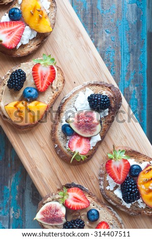 Healthy fruit topped open sandwich of Wholemeal rye bread with strawberry, blackberry, grilled peach and fig. Served on a wooden board.