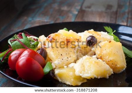 Bacalhau com natas. A Portuguese Brazilian dish of salt cod cooked with potatoes, cream and olives. Served with tomatoes and fresh salad leaves.