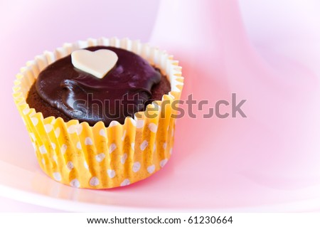 Freshly baked cupcake topped with chocolate icing and a white chocolate heart.