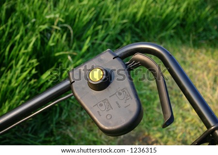 Handle of a lawnmower with the start button and some grass background.