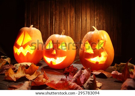 Jack o lanterns Halloween pumpkin face on wooden background and autumn leafs