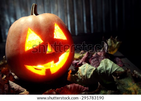 Jack o lanterns Halloween pumpkin face on wooden background and autumn leafs