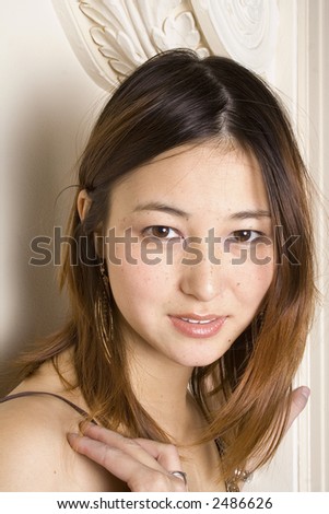 Soft lighting highlights the skin tones of this young Asian woman who is looking intently at the camera.