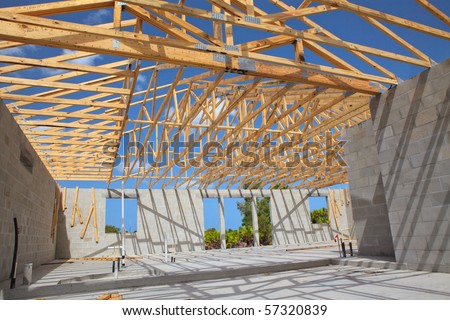 New home Construction of a cement block home with wooden roof trusses view from inside.