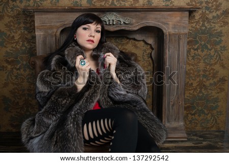 Charming dark-haired lady wearing fur coat and sitting in a vintage room