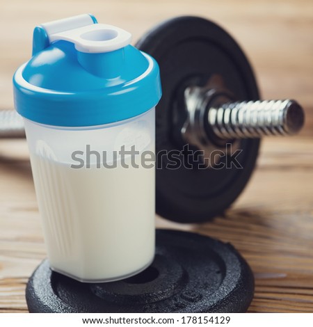 Shaker with protein drink and a dumbbell, close-up