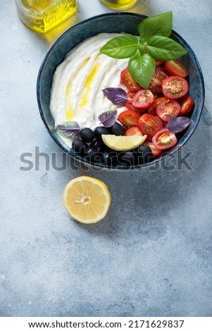 Bowl of greek tarama dip with olives, cherry tomatoes and fresh basil leaves, elevated view on a light-blue stone background, vertical shot with space Stok fotoğraf © 